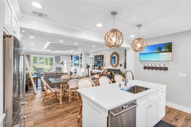 kitchen with a center island with sink, sink, white cabinetry, hanging light fixtures, and appliances with stainless steel finishes