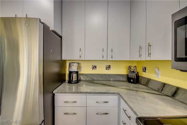 kitchen featuring light stone countertops, white cabinets, stainless steel fridge, and stove