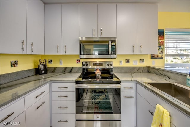 kitchen with light stone countertops, white cabinetry, sink, and stainless steel appliances