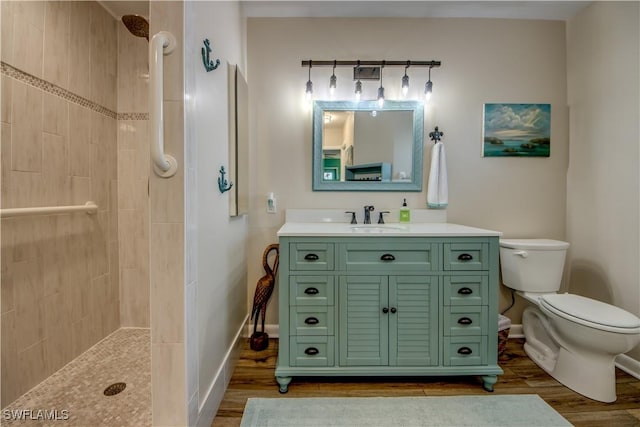 bathroom with toilet, vanity, tiled shower, and hardwood / wood-style floors