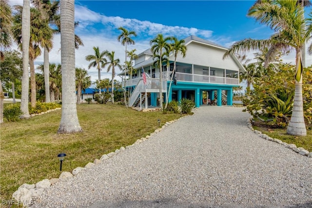 raised beach house with a front yard, a sunroom, and a carport