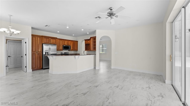 kitchen featuring ceiling fan with notable chandelier, pendant lighting, a kitchen island, a kitchen bar, and stainless steel appliances