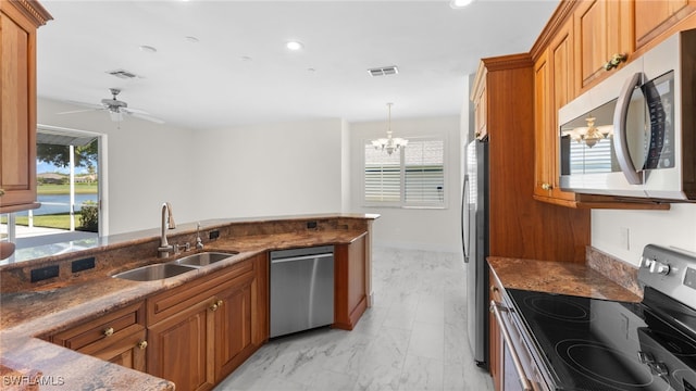 kitchen featuring ceiling fan with notable chandelier, stainless steel appliances, dark stone countertops, sink, and hanging light fixtures