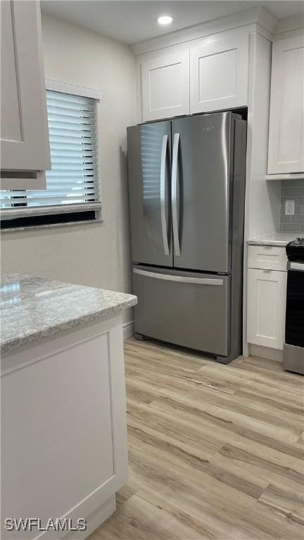 kitchen featuring light hardwood / wood-style flooring, appliances with stainless steel finishes, white cabinetry, light stone counters, and decorative backsplash