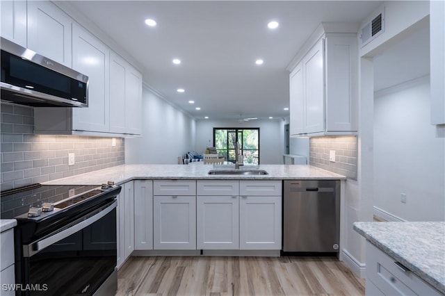 kitchen featuring white cabinetry, sink, kitchen peninsula, stainless steel appliances, and light wood-type flooring