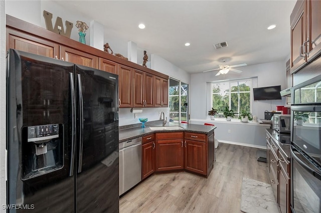 kitchen featuring ceiling fan, dark stone countertops, black appliances, sink, and light hardwood / wood-style flooring