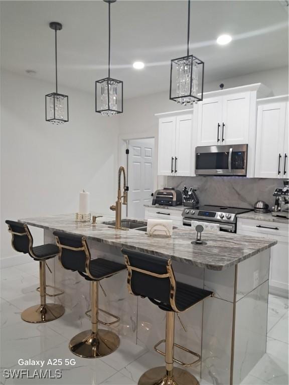 kitchen with an island with sink, stainless steel appliances, backsplash, decorative light fixtures, and white cabinets