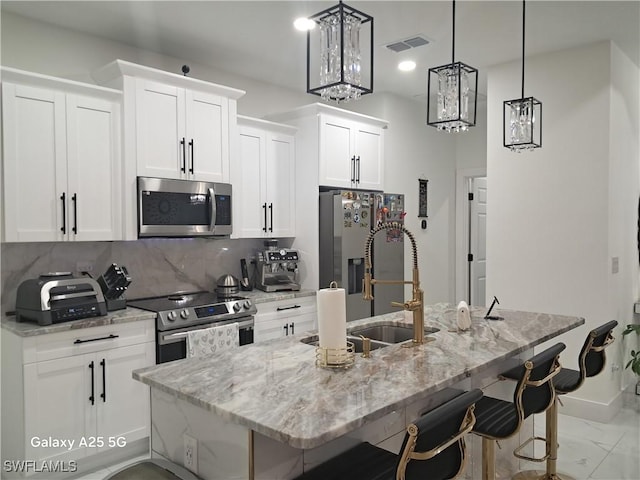 kitchen featuring stainless steel appliances, a kitchen island with sink, a kitchen breakfast bar, pendant lighting, and white cabinets