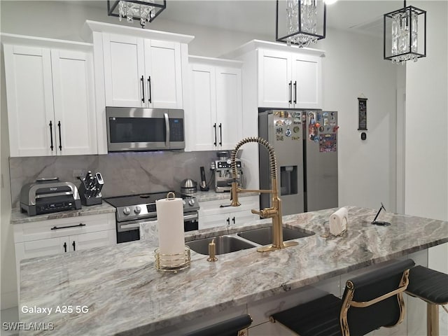 kitchen featuring appliances with stainless steel finishes, white cabinets, tasteful backsplash, and decorative light fixtures