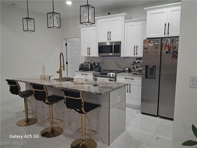 kitchen with appliances with stainless steel finishes, white cabinetry, backsplash, hanging light fixtures, and a center island with sink