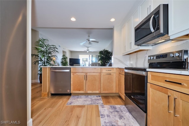 kitchen with kitchen peninsula, appliances with stainless steel finishes, white cabinetry, and light hardwood / wood-style flooring