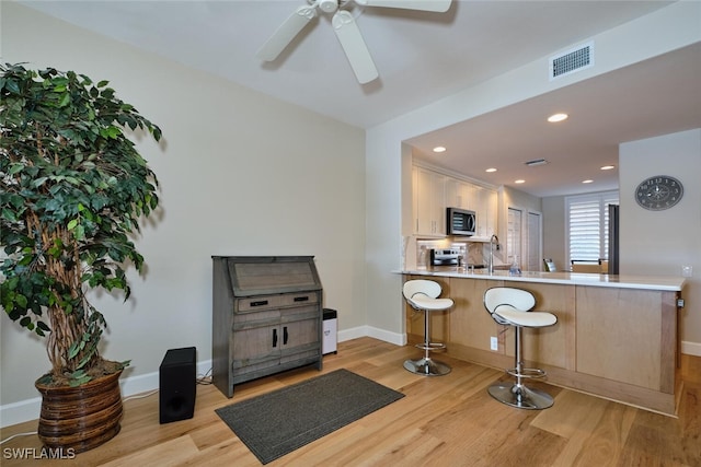 kitchen featuring stainless steel appliances, light hardwood / wood-style floors, sink, kitchen peninsula, and a breakfast bar