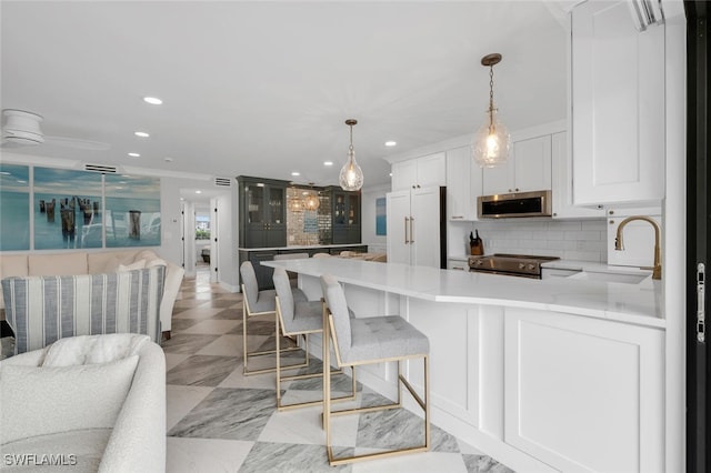 kitchen featuring a kitchen bar, appliances with stainless steel finishes, decorative backsplash, hanging light fixtures, and white cabinets