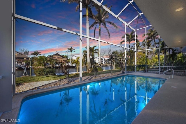 pool at dusk with a patio, glass enclosure, and a water view