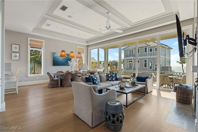 living room with a raised ceiling, plenty of natural light, and light hardwood / wood-style floors