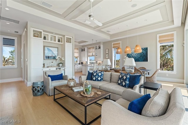 living room featuring ceiling fan, a raised ceiling, and light wood-type flooring