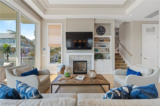 living room with a tray ceiling, a fireplace, built in features, and light wood-type flooring