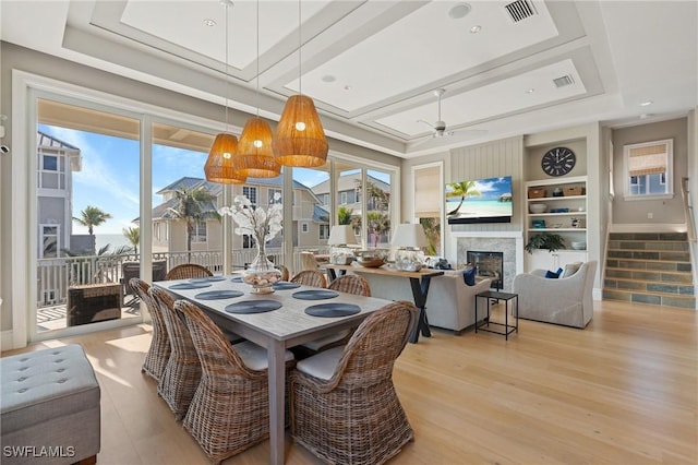 dining space featuring ceiling fan, a tray ceiling, built in features, and light wood-type flooring