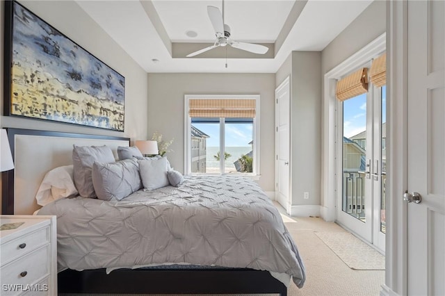 carpeted bedroom featuring access to exterior, a tray ceiling, and ceiling fan