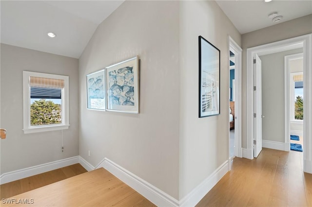 corridor featuring lofted ceiling, a healthy amount of sunlight, and light hardwood / wood-style floors