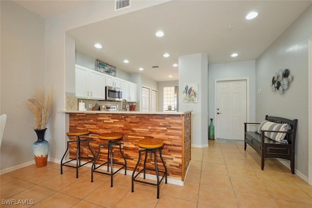 kitchen with white cabinetry, backsplash, kitchen peninsula, light tile patterned floors, and a breakfast bar area