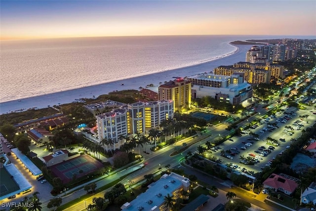 aerial view at dusk featuring a water view and a view of the beach