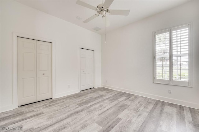 unfurnished bedroom featuring multiple closets, ceiling fan, multiple windows, and light hardwood / wood-style flooring