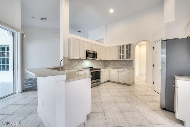 kitchen featuring appliances with stainless steel finishes, sink, backsplash, light tile patterned floors, and kitchen peninsula