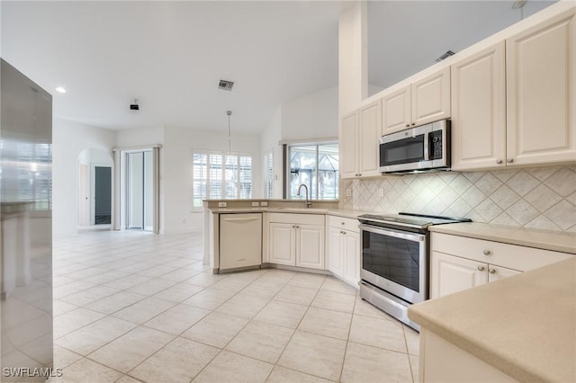 kitchen with vaulted ceiling, light tile patterned floors, appliances with stainless steel finishes, pendant lighting, and backsplash