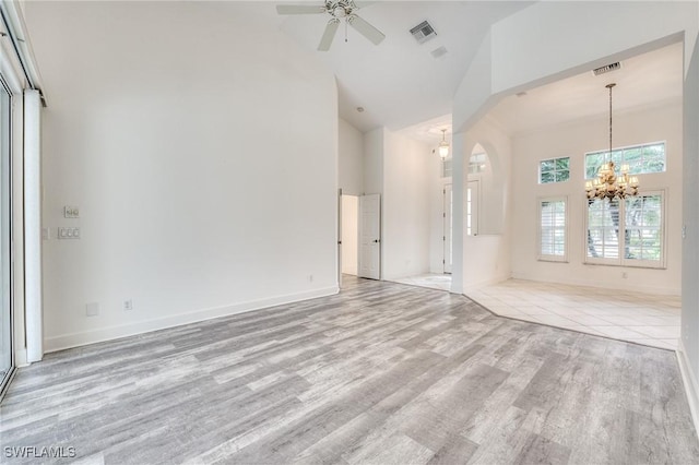 unfurnished living room with ceiling fan with notable chandelier, high vaulted ceiling, and light hardwood / wood-style floors