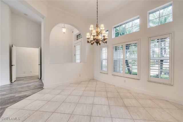 tiled empty room featuring a high ceiling, crown molding, and a chandelier