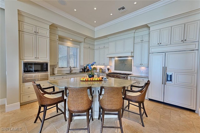 kitchen with built in appliances, light stone countertops, an island with sink, and a breakfast bar area