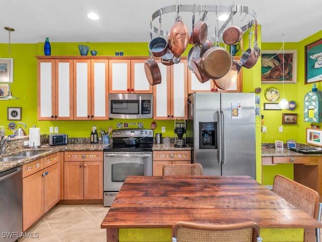 kitchen featuring stainless steel appliances, decorative light fixtures, light tile patterned flooring, dark stone countertops, and sink