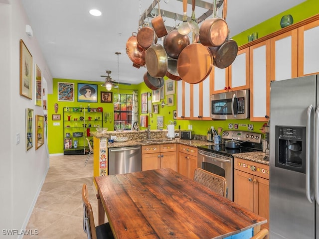 kitchen with ceiling fan, dark stone countertops, kitchen peninsula, appliances with stainless steel finishes, and light tile patterned floors