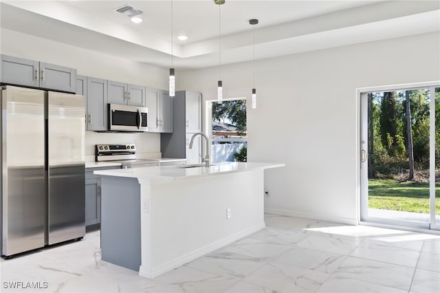 kitchen featuring sink, hanging light fixtures, appliances with stainless steel finishes, and an island with sink