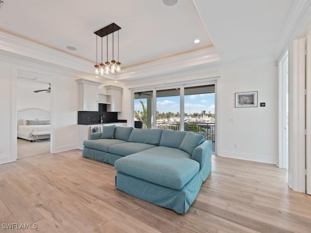 living room with an inviting chandelier, light hardwood / wood-style floors, sink, a tray ceiling, and crown molding