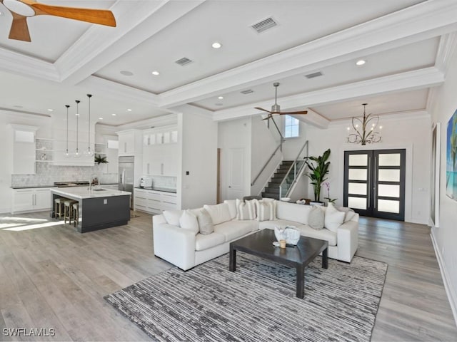 living room with crown molding, light hardwood / wood-style flooring, french doors, ceiling fan with notable chandelier, and beamed ceiling