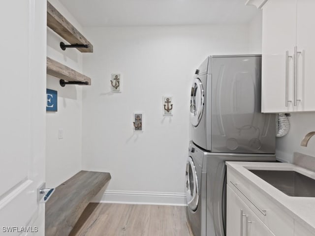 clothes washing area with sink, stacked washing maching and dryer, light hardwood / wood-style floors, and cabinets