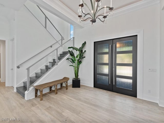 entrance foyer with ornamental molding, light wood-type flooring, a notable chandelier, and french doors