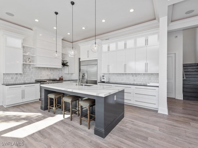 kitchen featuring built in refrigerator, white cabinetry, and an island with sink