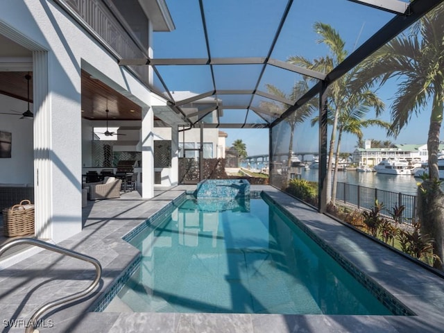 view of swimming pool featuring an outdoor kitchen, a patio, glass enclosure, a water view, and ceiling fan