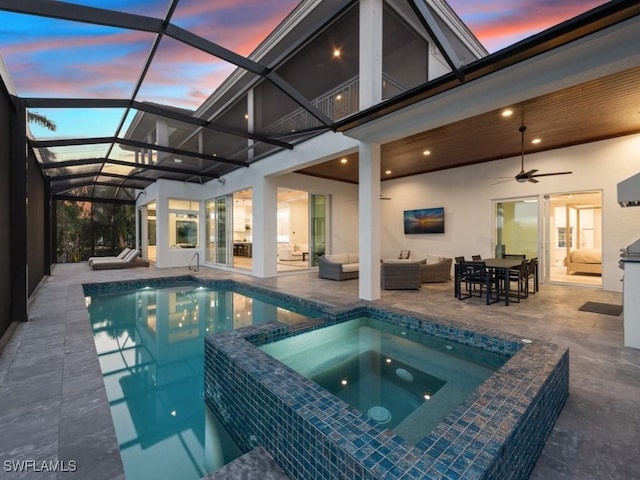 pool at dusk featuring glass enclosure, an in ground hot tub, a patio area, outdoor lounge area, and ceiling fan