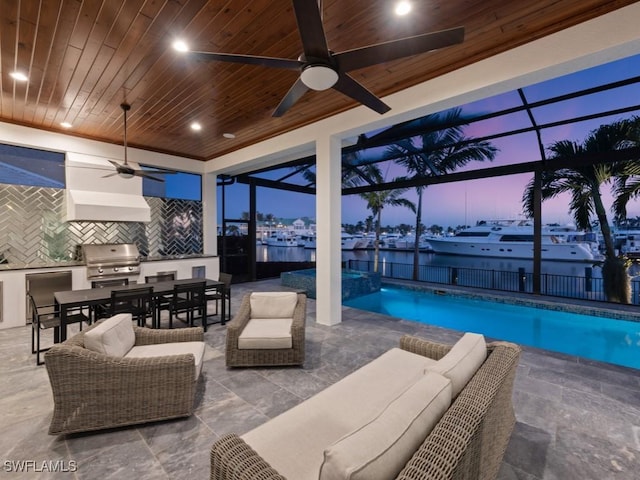 pool at dusk featuring glass enclosure, a patio area, a grill, ceiling fan, and area for grilling