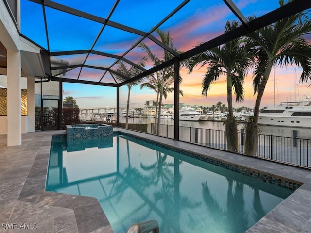 pool at dusk featuring glass enclosure, a patio area, an in ground hot tub, and a water view