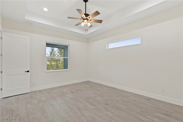 empty room with ceiling fan, light wood-type flooring, and a tray ceiling