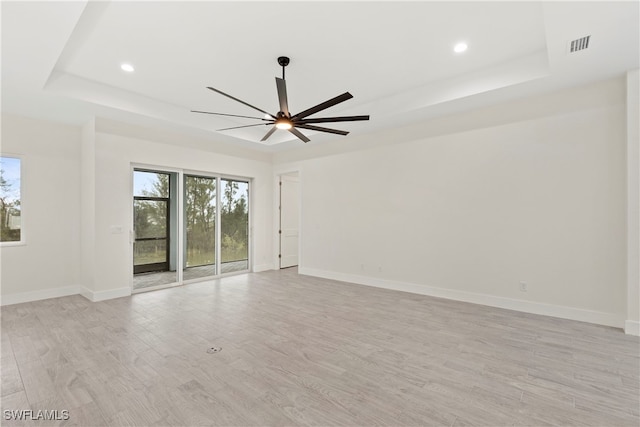 spare room featuring ceiling fan, light wood-type flooring, and a tray ceiling