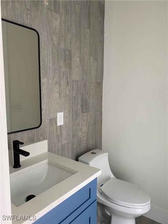 bathroom with toilet, vanity, and wooden walls