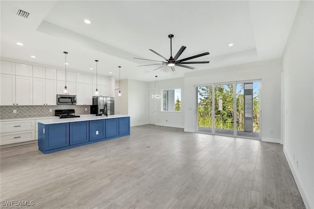 kitchen with white cabinets, appliances with stainless steel finishes, an island with sink, hanging light fixtures, and a tray ceiling