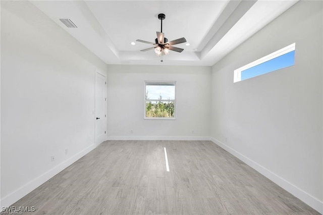 spare room with light wood-type flooring, ceiling fan, and a raised ceiling