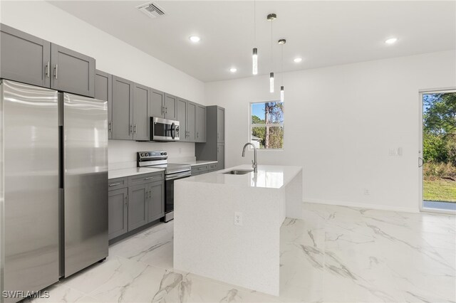 kitchen featuring decorative light fixtures, gray cabinets, sink, an island with sink, and stainless steel appliances